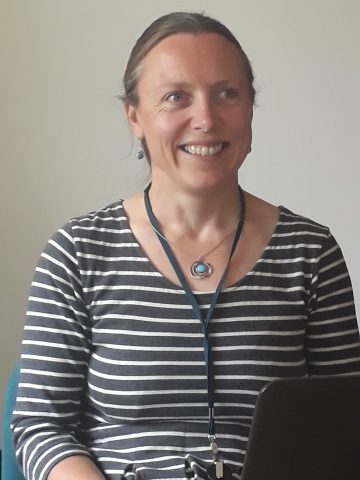 Photograph of Dr Alison Fox. A white woman wearing a black-and-white striped top, a necklace and a lanyard. 