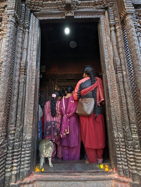 Image shows women in Nepalese clothing entering a religious space.